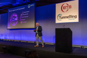 Man on stage with BTS and Tunnelling Journal logos in the background